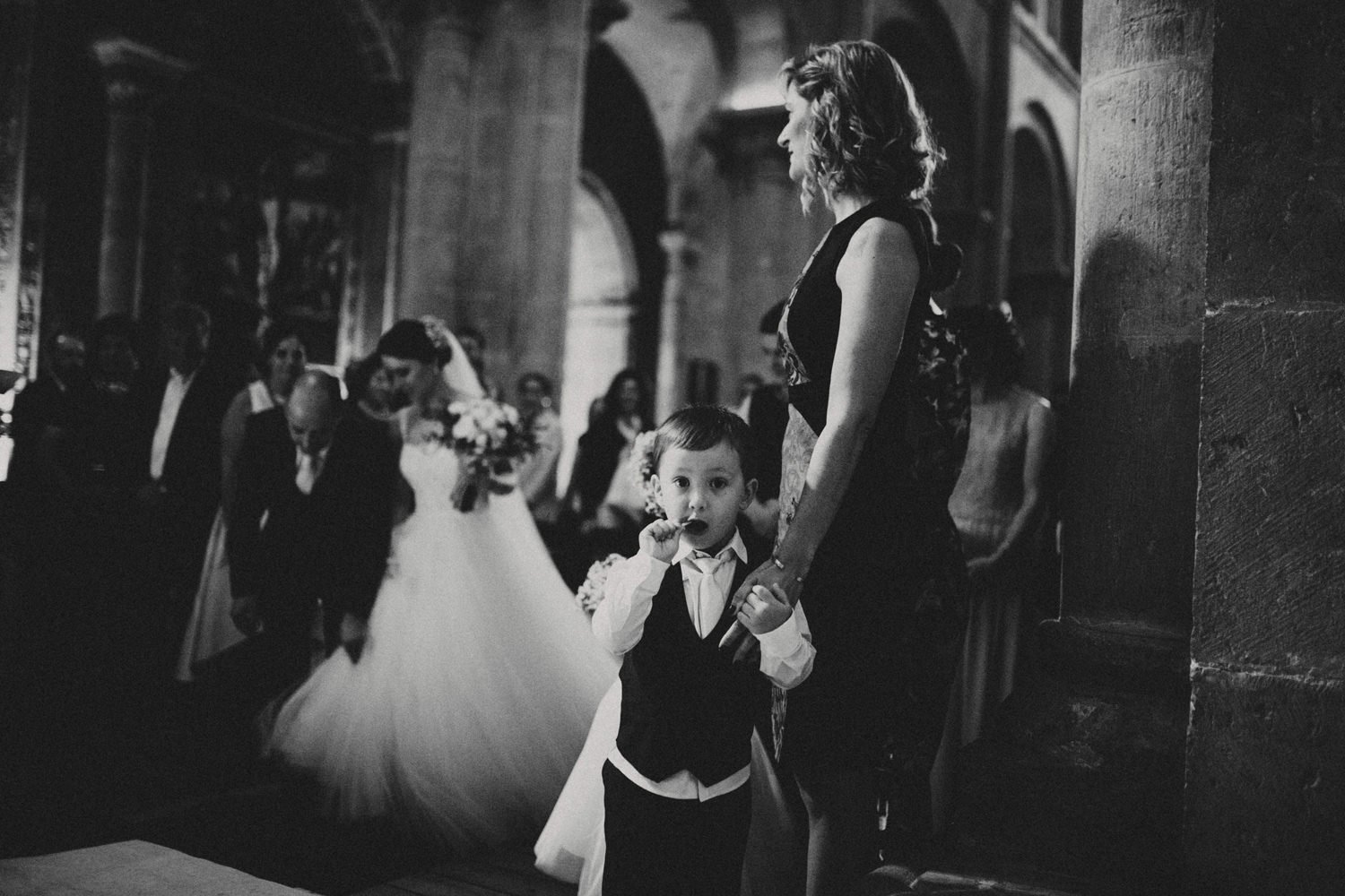 pageboy eating lollipop while bride and her father walks down the aisle in a wedding ceremony in coimbra portugal